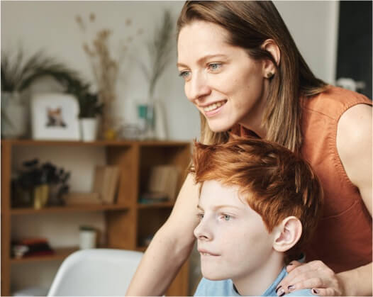 adult woman with light colored skin and brown hair and orange shirt. Child male with light colored skin, reddish short hair sitting in front of woman.